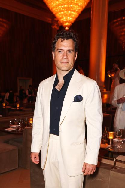 Henry Cavill in a cream suit and dark blue shirt.