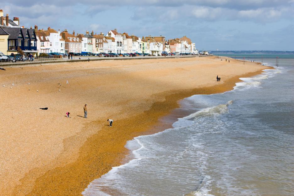 The shingle beach and seafront in Deal, Kent, lined with houses and cars.