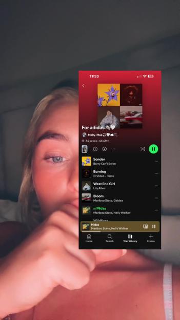 A woman looking at her phone displaying a Spotify playlist titled "For adidas," featuring the song "Midas" by Maribou State and Holly Walker.