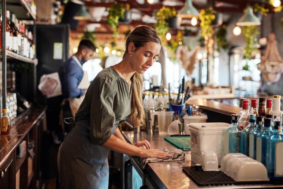 A waitress in an apron wiping down a restaurant counter.