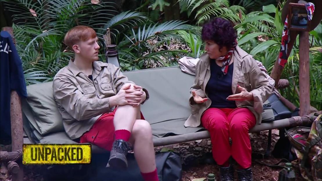 Two people sit on a bench in a jungle setting.