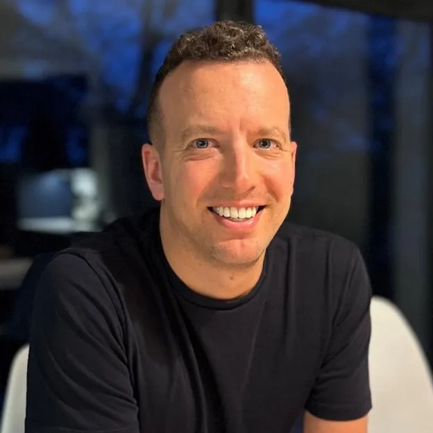 A portrait of a smiling man wearing a black t-shirt.