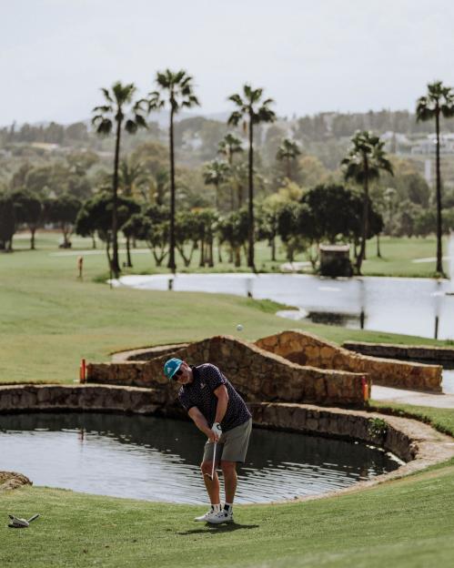 A golfer hitting a ball over water on a golf course at Los Naranjos Golf Club.