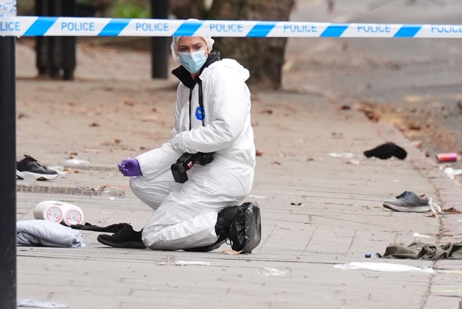 A forensic investigator in a white suit and mask kneels at a crime scene, which is cordoned off with "POLICE" tape.
