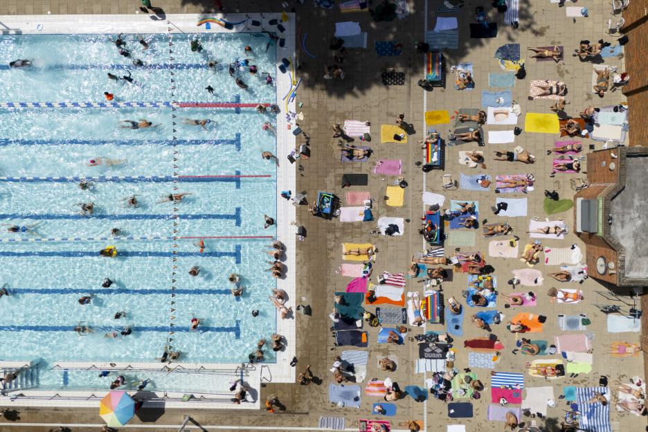 Aerial view of people swimming and sunbathing at an outdoor swimming pool during a heatwave.
