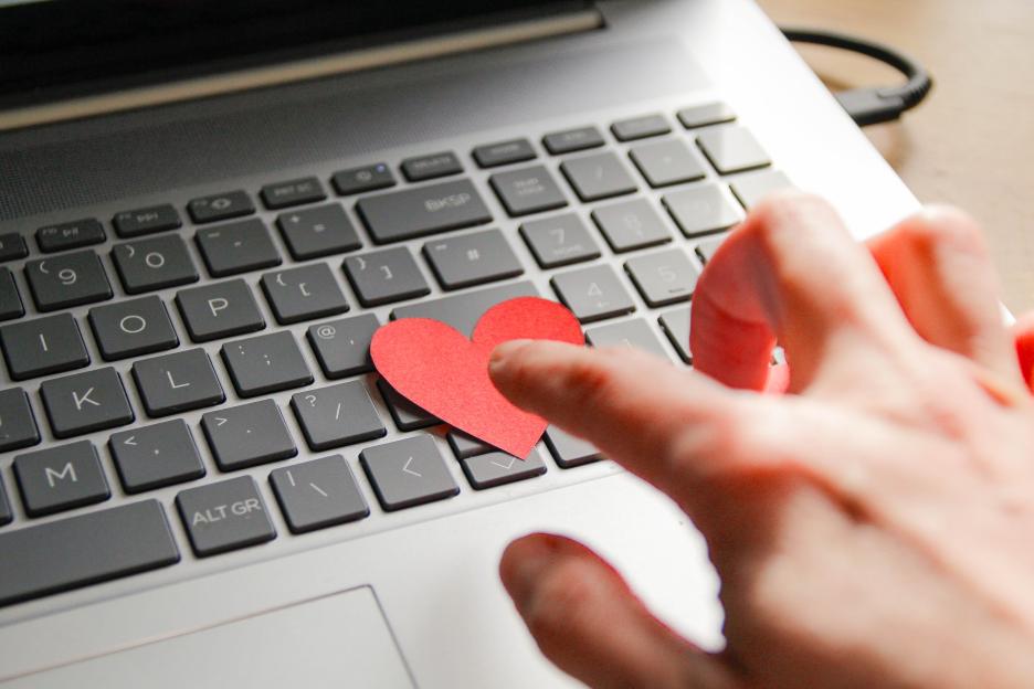 Hand placing a red heart on a laptop keyboard.