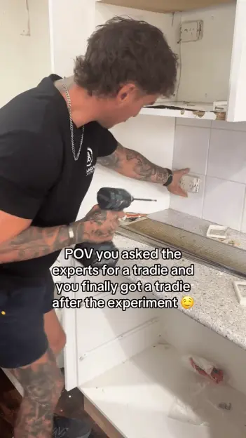 A man with tattoos holding a drill while working on kitchen cabinets.