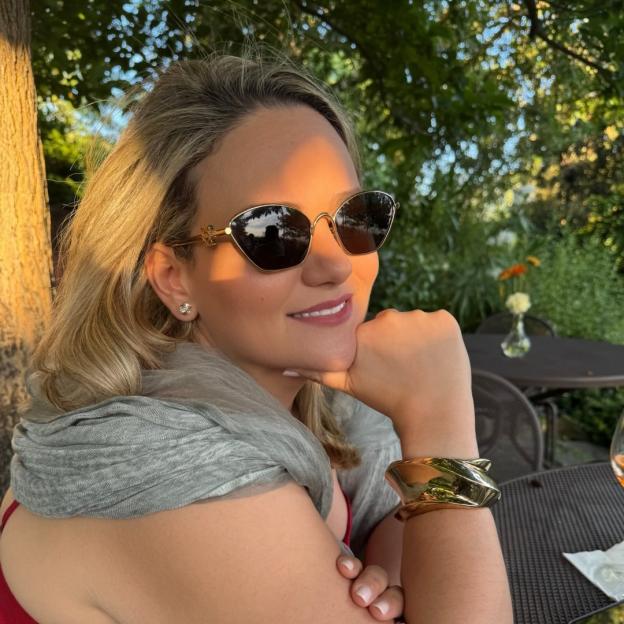 Lorna Hajdini, a blond woman in sunglasses, smiling with her chin resting on her hand.