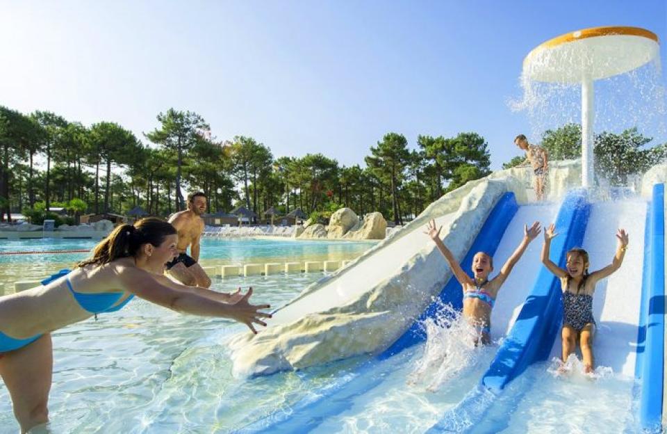 Children splashing down a water slide as adults watch from the pool.