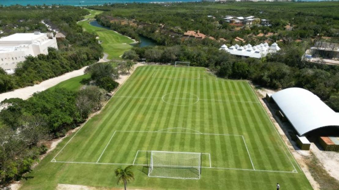 Aerial view of a soccer field with striped grass next to a luxury hotel and golf course.