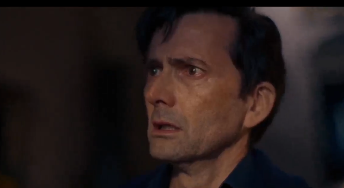 A man with dark hair looks on with a concerned expression.