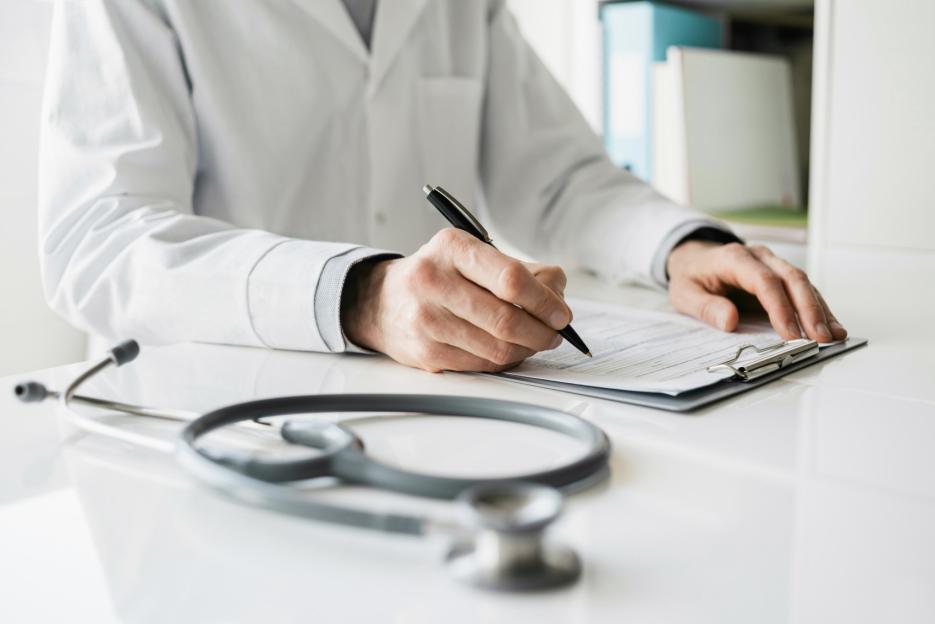 Doctor writing notes on a clipboard with a stethoscope in the foreground.