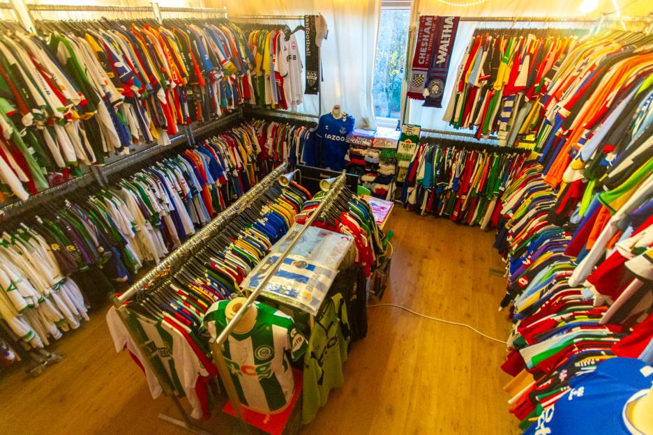 A shop with walls lined with many rows of colorful football shirts.