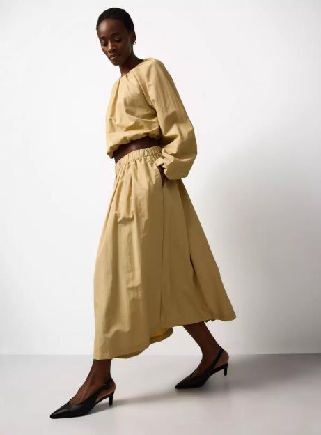 A model wearing a beige crop top with voluminous sleeves and a matching elasticated waist skirt.