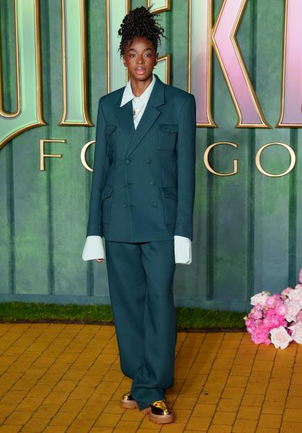 Cat Burns wearing a dark teal suit with a white shirt and leopard-print shoes at the European premiere of Wicked: For Good.