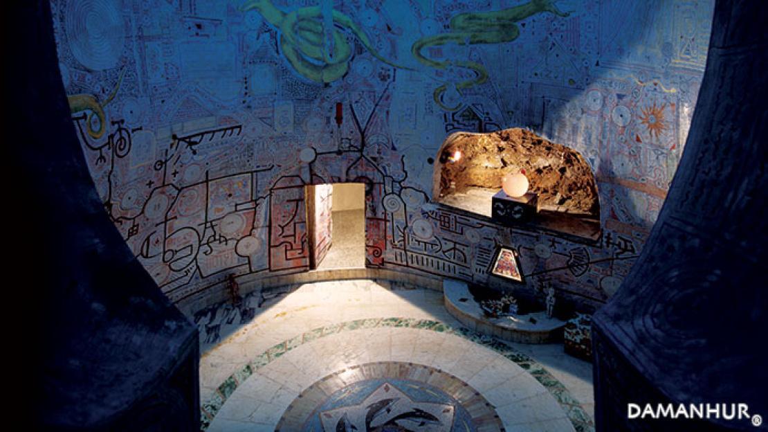 The Damanhur Sala dell'Acqua with intricate murals on the walls and ceiling, a circular mosaic floor, and a glowing orb in a rock niche.