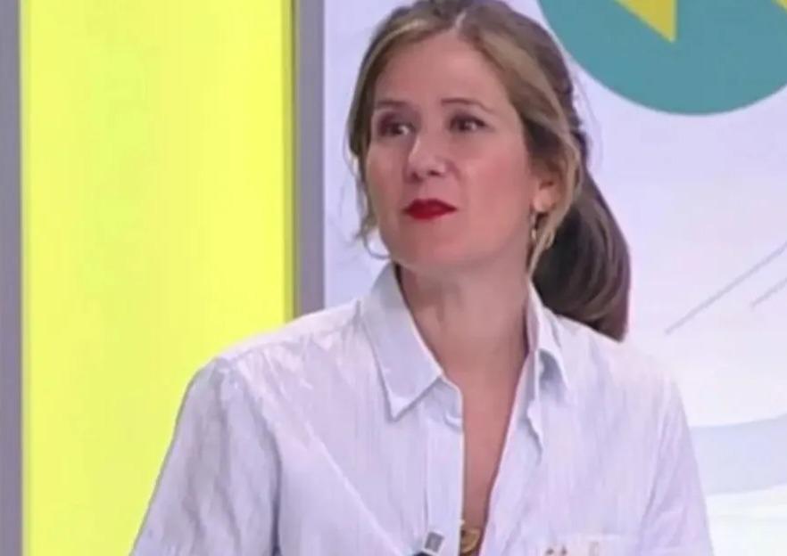 María José Fuenteálamo, a woman with long, light brown hair pulled back, wearing a light blue button-down shirt and red lipstick, looks to her right.