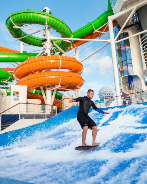 A man on Royal Caribbean's Liberty of the Seas cruise ship, surfing on an artificial wave with water slides in the background.