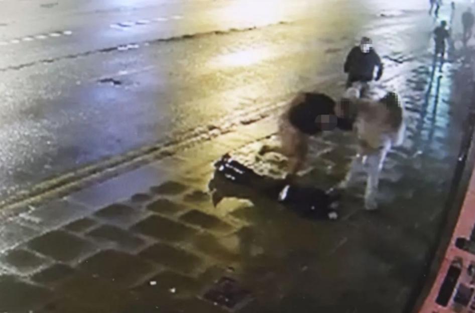 Security camera footage captures three blurred figures in an altercation on a wet street.