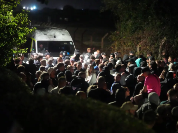 A crowd of people gathered at night with a white van in the background.