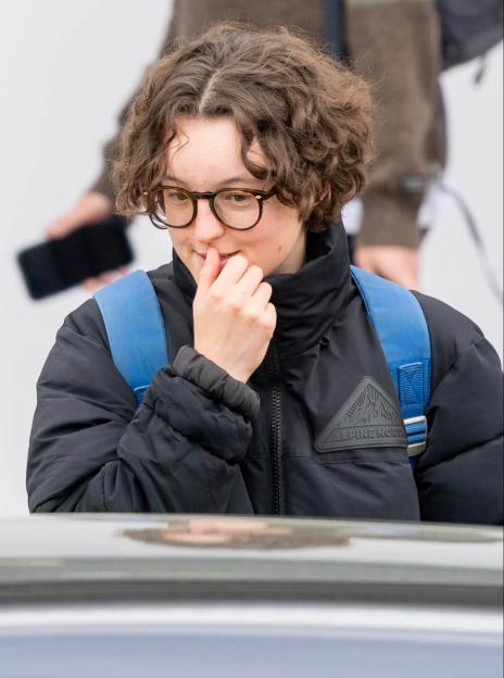Bella Ramsey wearing a black puffer jacket and glasses, with a blue backpack, arriving in Inverness.