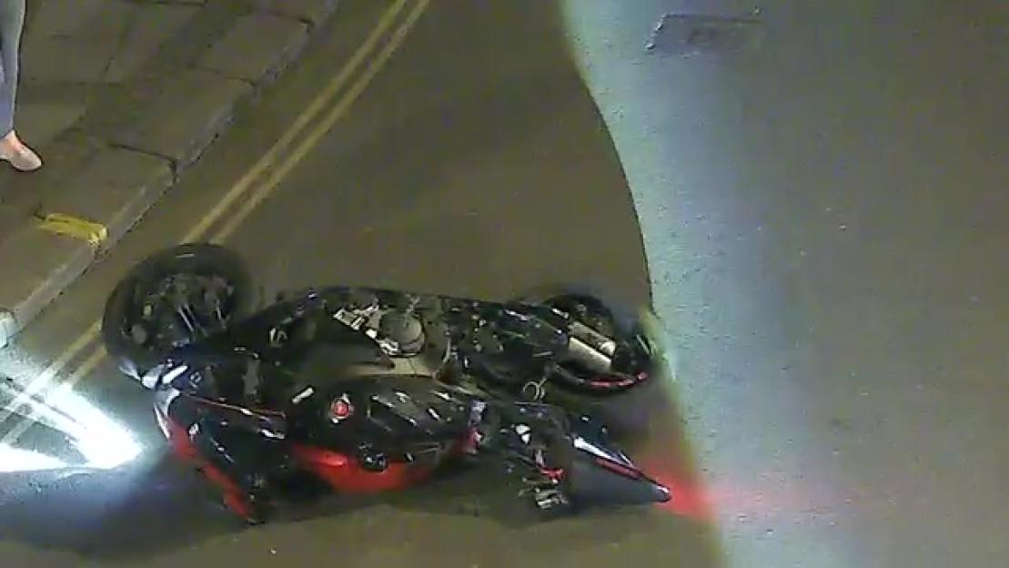 Motorcycle crashed and lying on its side on a dark road with double yellow lines.
