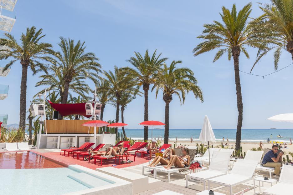 Ushuaia Hotel and Club in Platja d'en Bossa, Ibiza, with people relaxing on lounge chairs by the pool and beach.