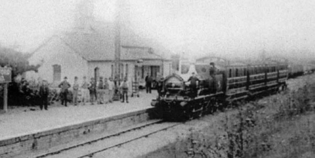 Black and white photo of a Victorian railway station with a train and people on the platform.