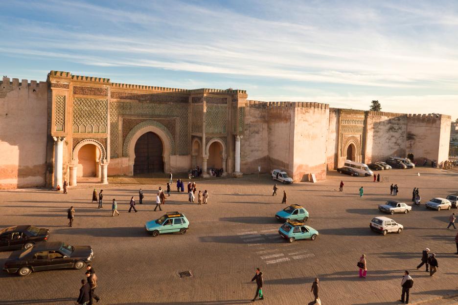 Bab Al Mansour gate in Meknes, Morocco, with people and cars in the foreground.