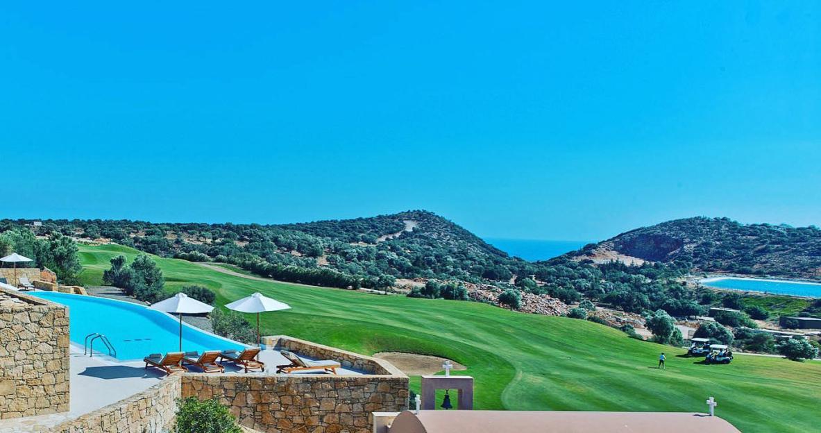 View of the Crete Golf Club in Hersonissos, with a pool in the foreground and the sea in the background.