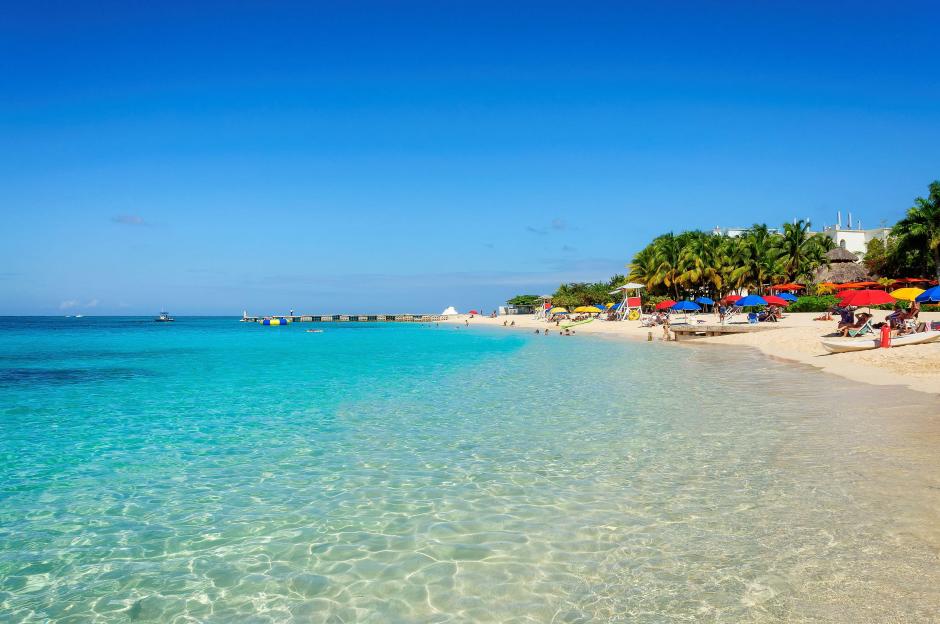 Tropical beach and sea in Jamaica with people relaxing under colorful umbrellas.
