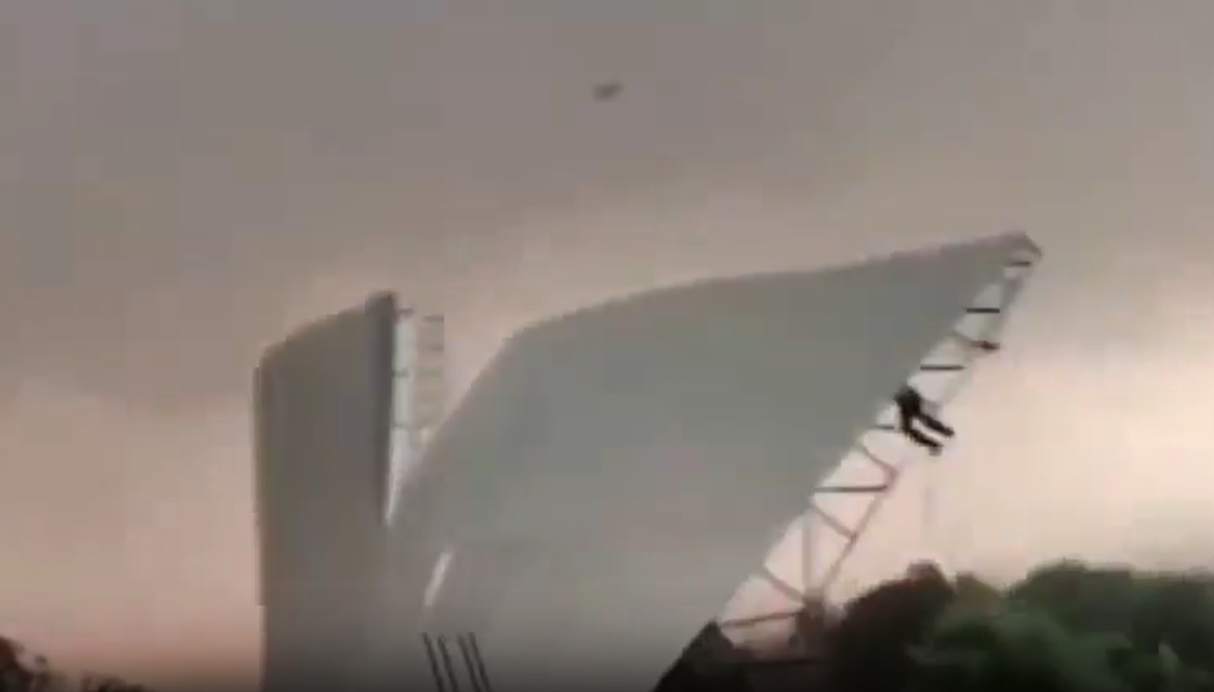 Man holding onto a metal roof as it is ripped off a building by strong winds.