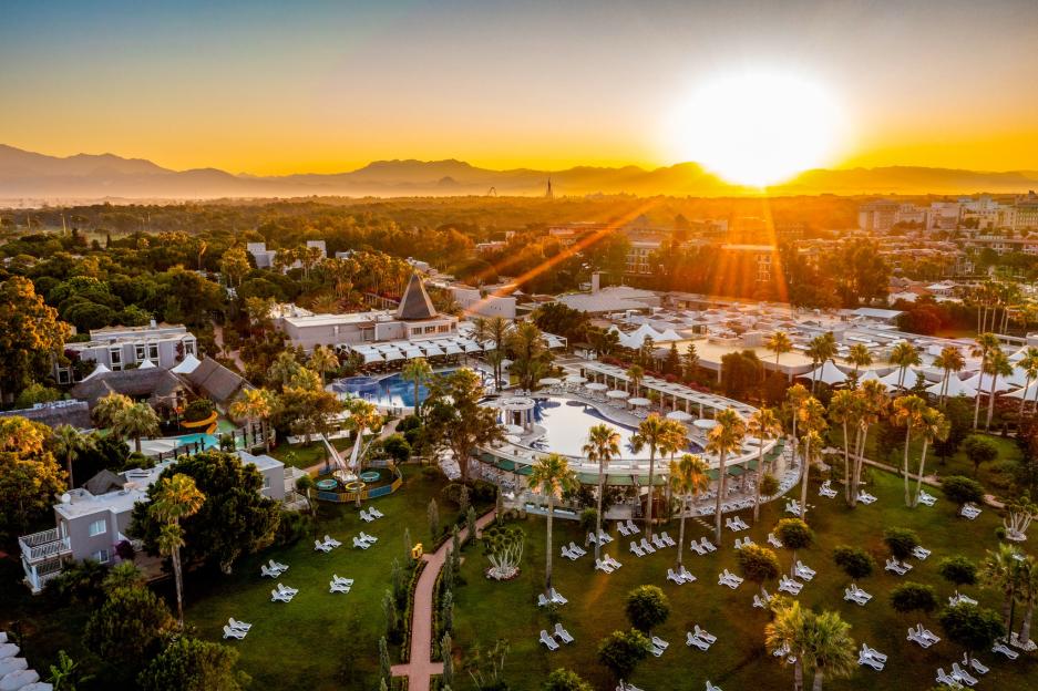 Aerial view of Tui Magic Life resort in Belek, Turkey, at sunset with palm trees, pools, and mountains in the background.