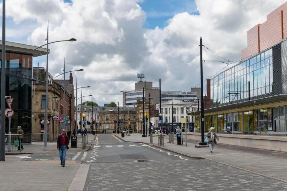 A view of Rochdale town centre in Greater Manchester, showing a paved street with modern and historic buildings under a partly cloudy sky.