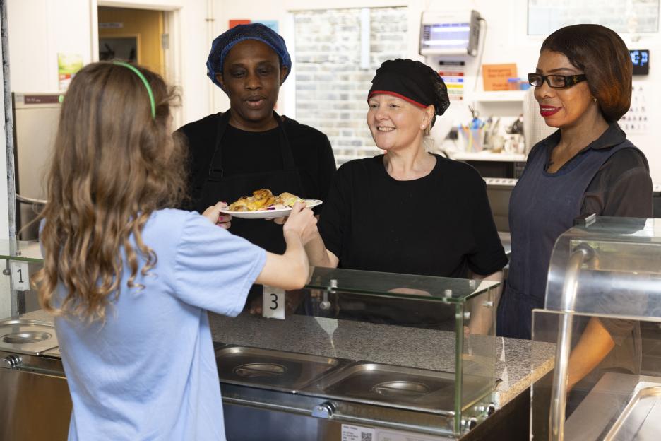 Tracey Nwabia, a school chef, and her two assistants, Abi and Stella, serving food to a student.