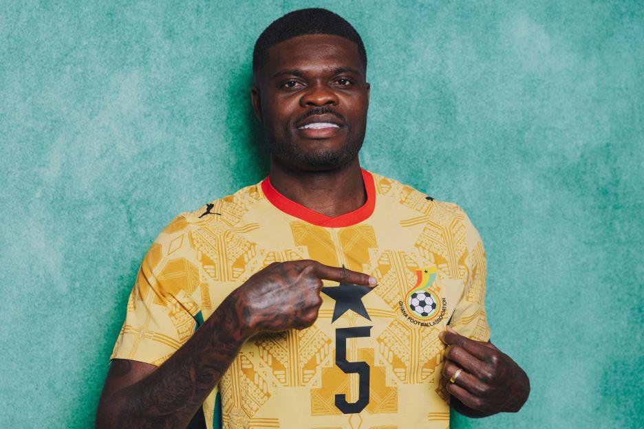 Thomas Partey poses for a portrait wearing a yellow Ghana football jersey with the number 5.