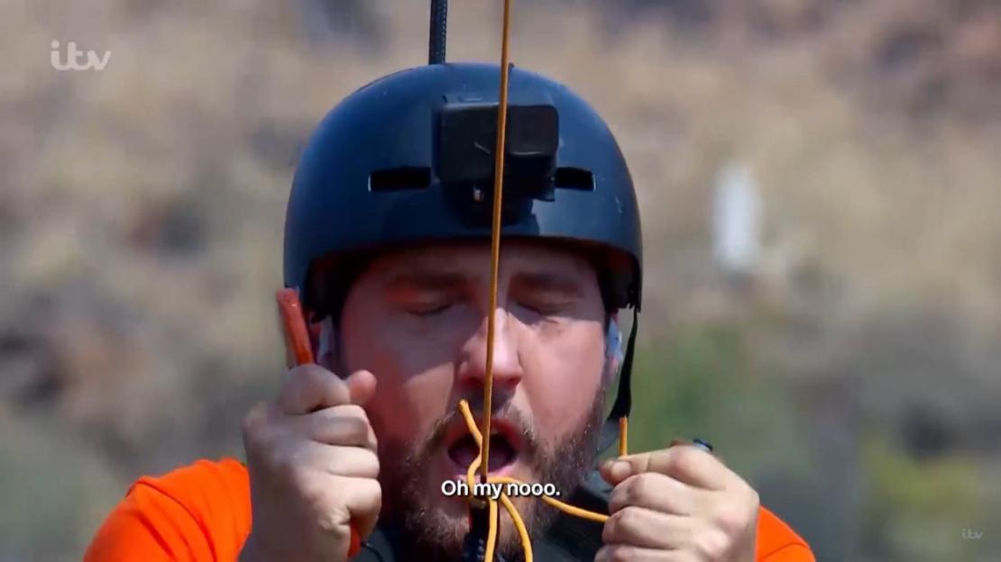 A man wearing a helmet and safety equipment with his eyes closed and rope in his mouth.