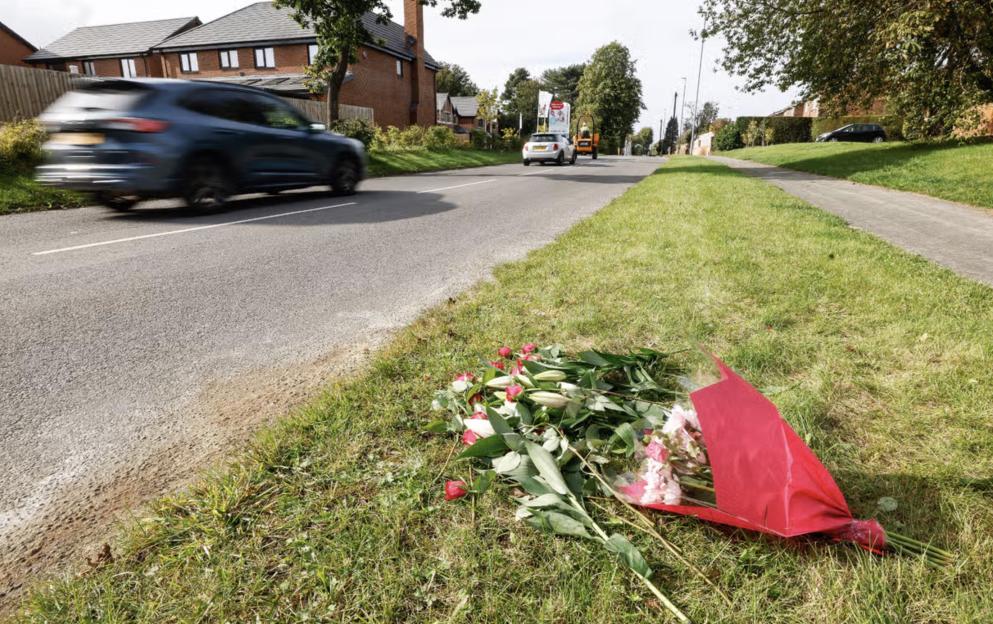 Flowers in red wrapping next to a road, where a car speeds past.