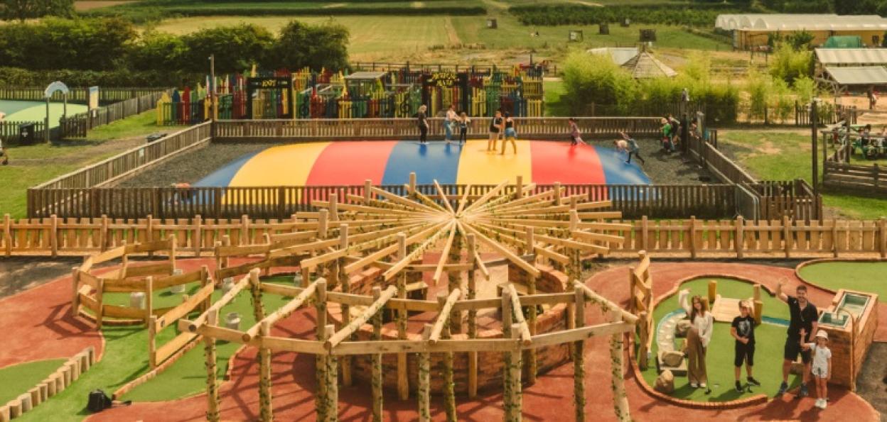 Overhead view of an adventure park with people on a colorful bouncy pad and families playing mini-golf.