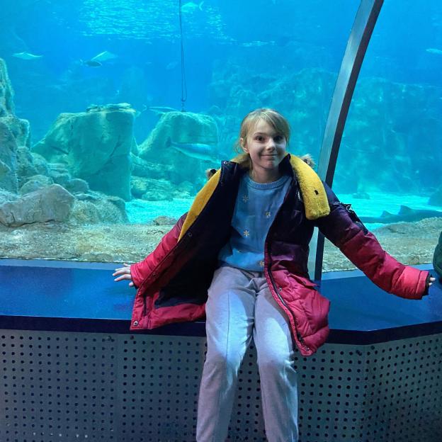 Lilia Valutyte, 9, sits in front of a large aquarium tank.