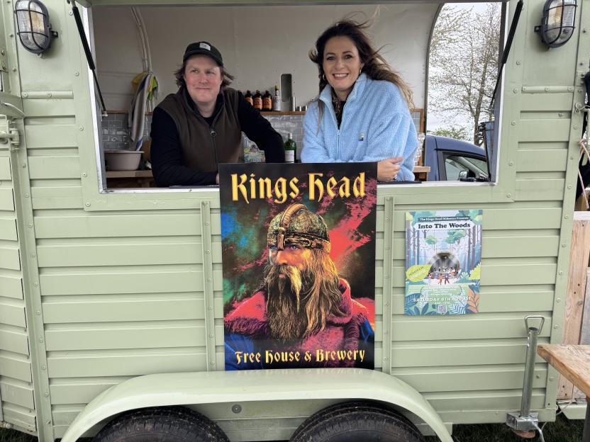 Two people smiling from the inside of a mobile pub, with a "Kings Head" sign depicting a Viking.