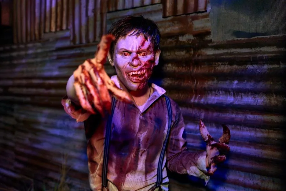 A scareactor dressed as a bloody zombie reaches out toward the camera at Halloween Horror Nights.