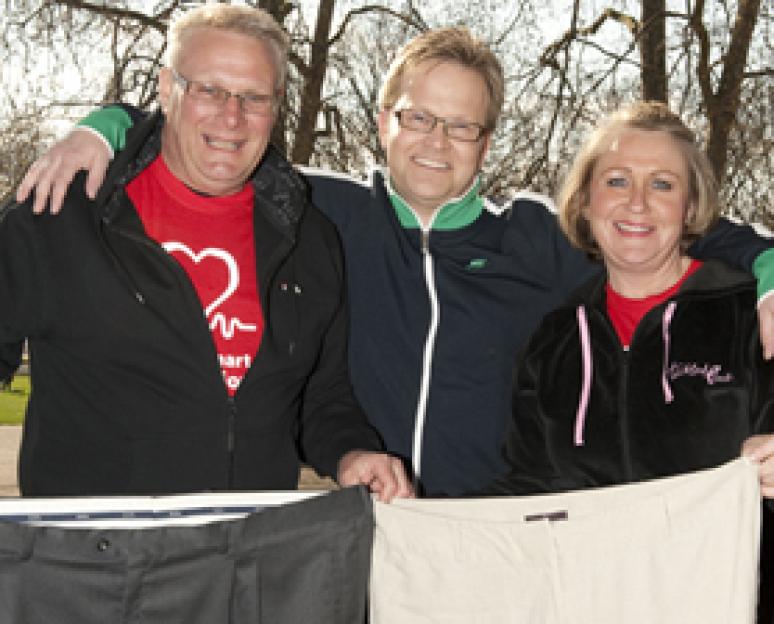 Phil Huzzey, Steve Miller, and Jan Huzzey holding up oversized trousers after a 10K walk for the British Heart Foundation.