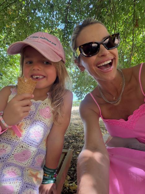 A young girl in a pink cap eating an ice cream cone next to a woman in sunglasses.