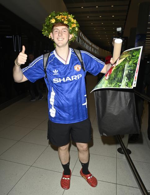 Internet personality Angry Ginge wearing a flower wreath, blue Manchester United jersey, and red Crocs, giving a thumbs-up.