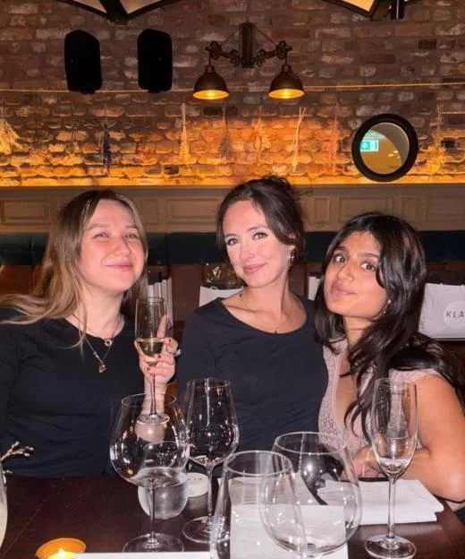 Three young women sitting together at a restaurant table with wine glasses and place cards.