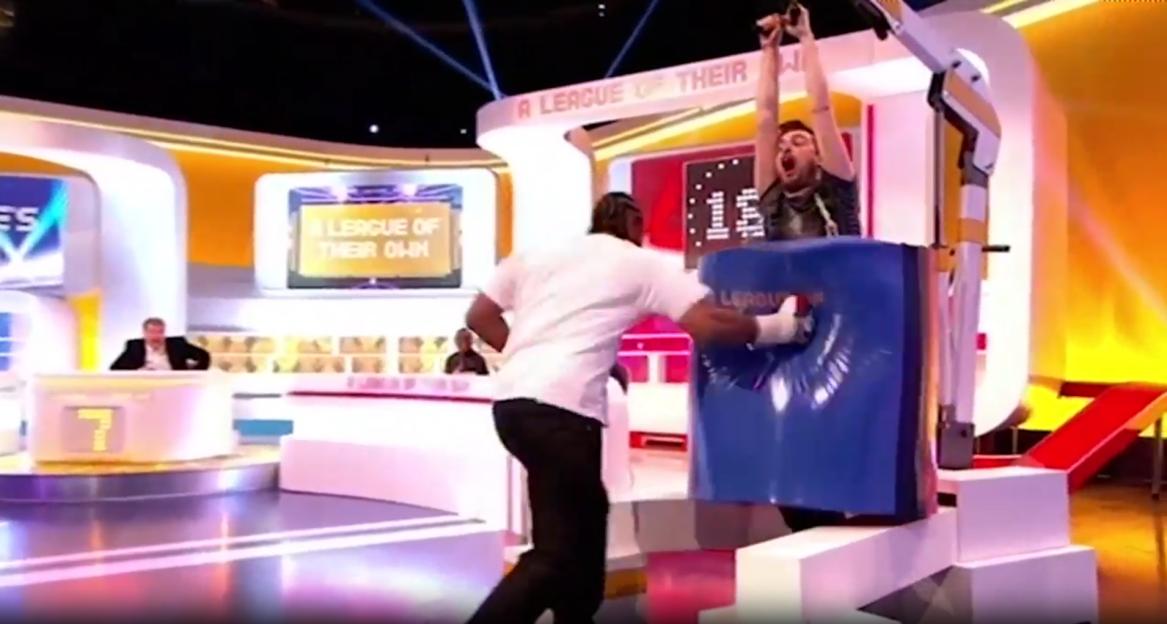 Two men participating in a game show, one punching a blue padded target and the other screaming with arms raised.