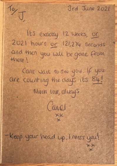 A handwritten letter on cardboard from "Cane" to "J" counting down the time until J is "gone from there," ending with "Keep your head up, I miss you!"