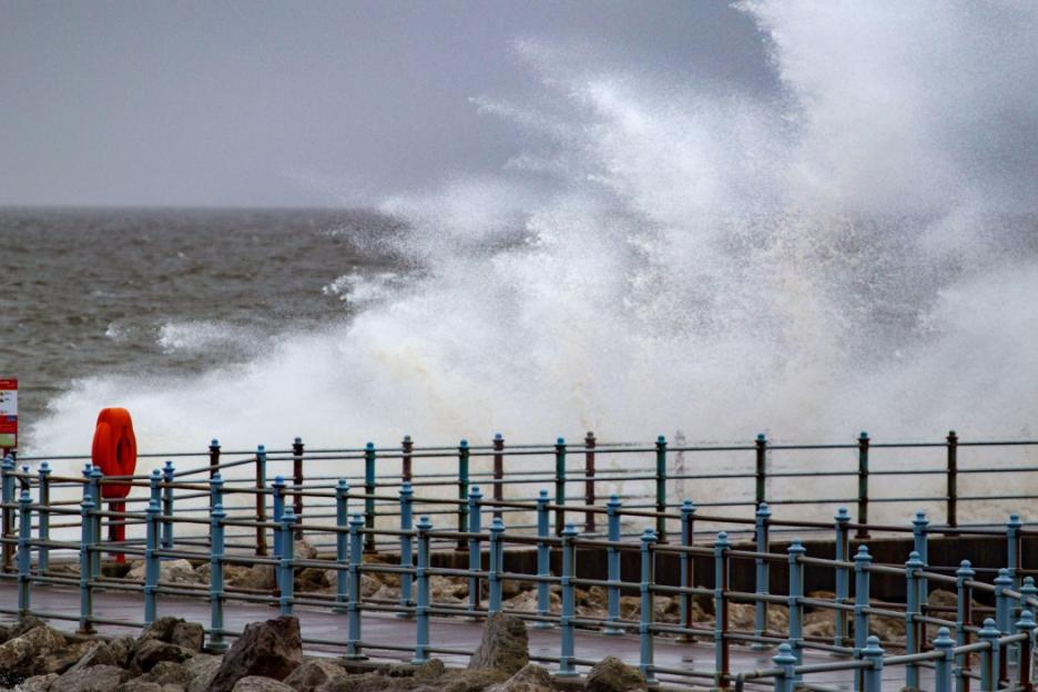 Large waves crashing onto the shore of Morecambe Bay, near a pier with an orange life buoy.