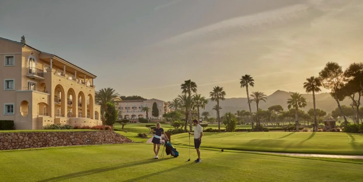 Two golfers stand on a lush green course next to a resort hotel at La Manga.